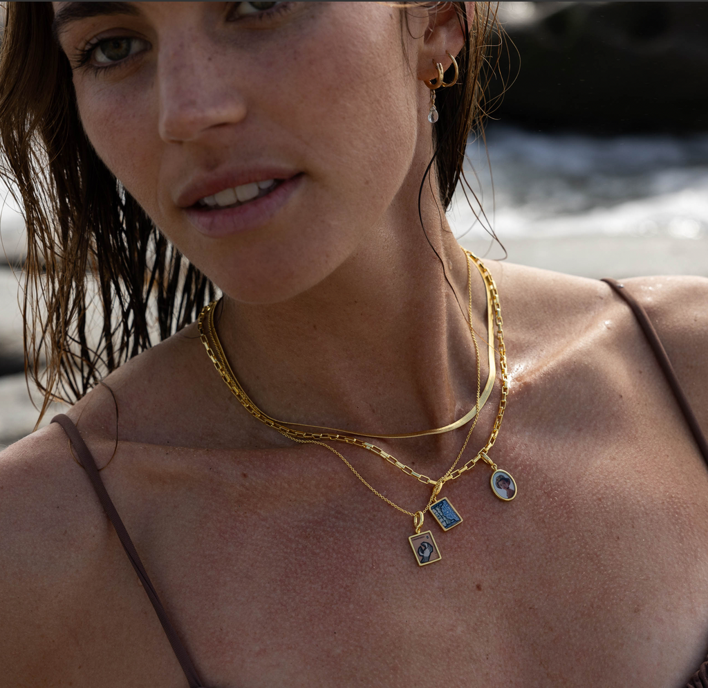 Woman wearing stacked charm necklaces with portrait and stamp charms